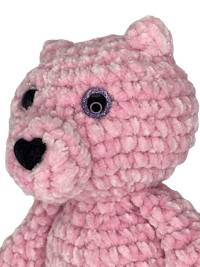 a pink crocheted teddy bear is shown against a black background