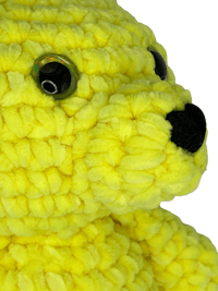 a yellow crocheted teddy bear on a black background