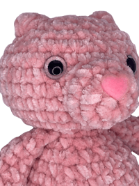 a pink crocheted teddy bear on a black background