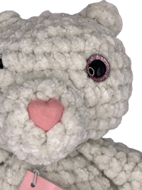 a white crocheted teddy bear with a pink tag