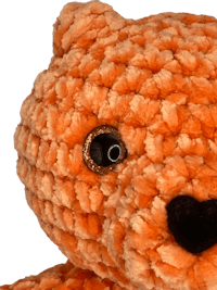 a crocheted orange teddy bear on a black background